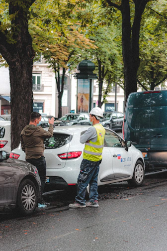 man in brown jacket standing beside white car during daytime