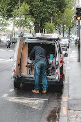 man in blue denim jeans and blue denim jeans standing on white van during daytime