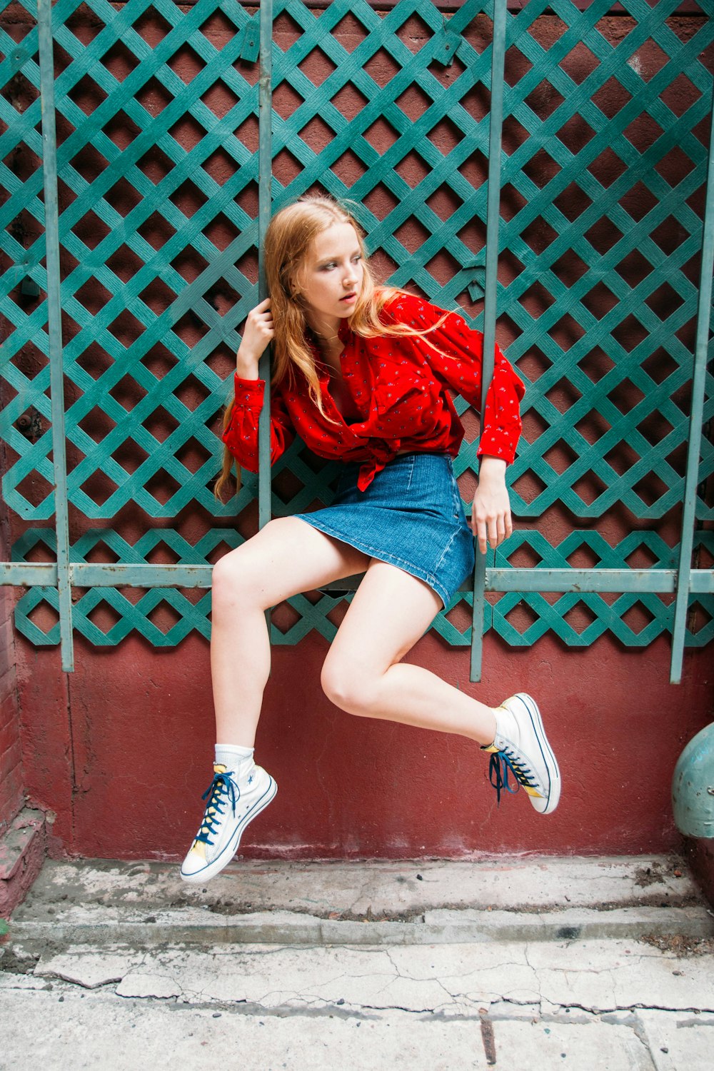 woman in red long sleeve shirt and blue denim shorts sitting on red metal fence