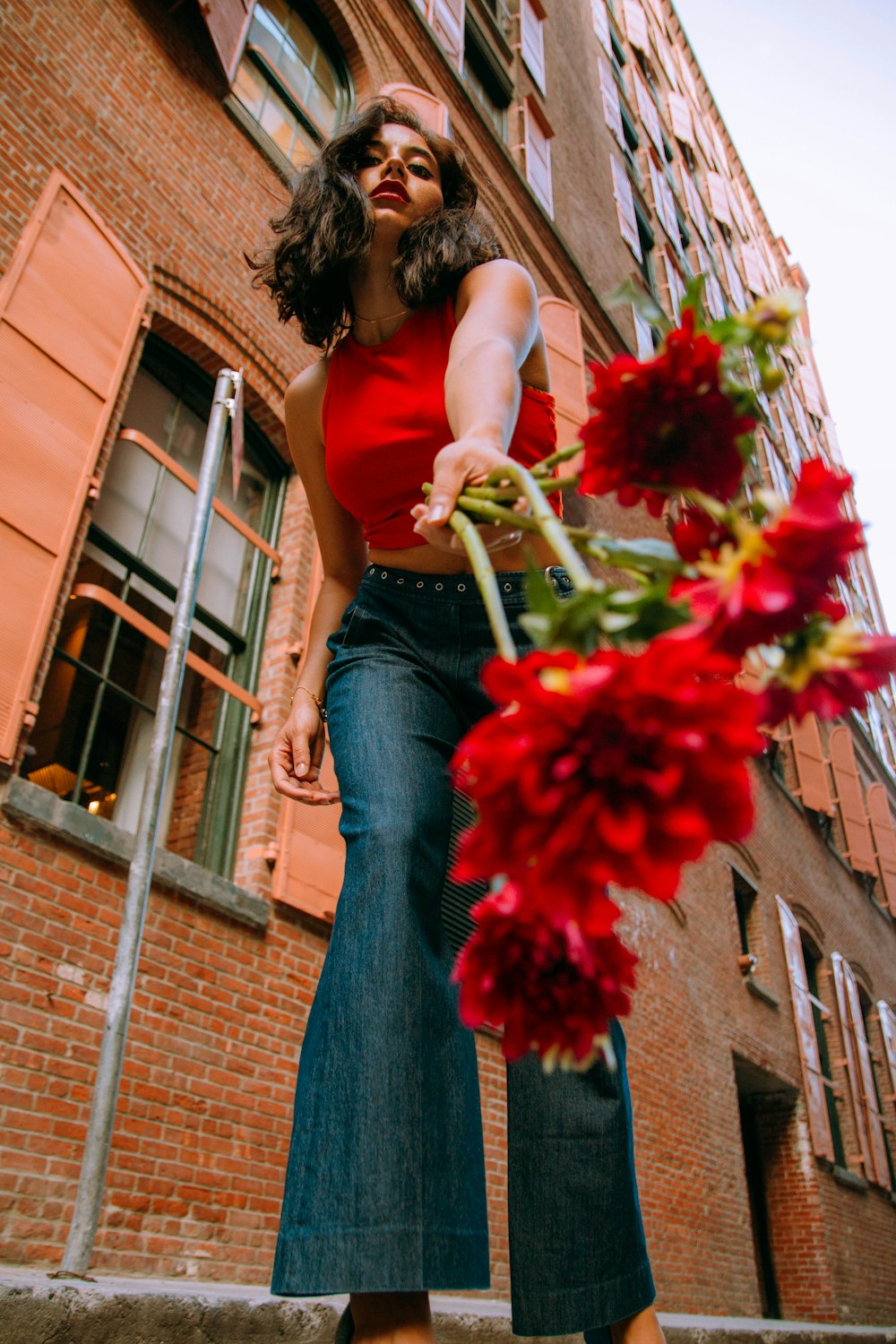 woman in red tank top and blue denim jeans holding red bouquet of flowers