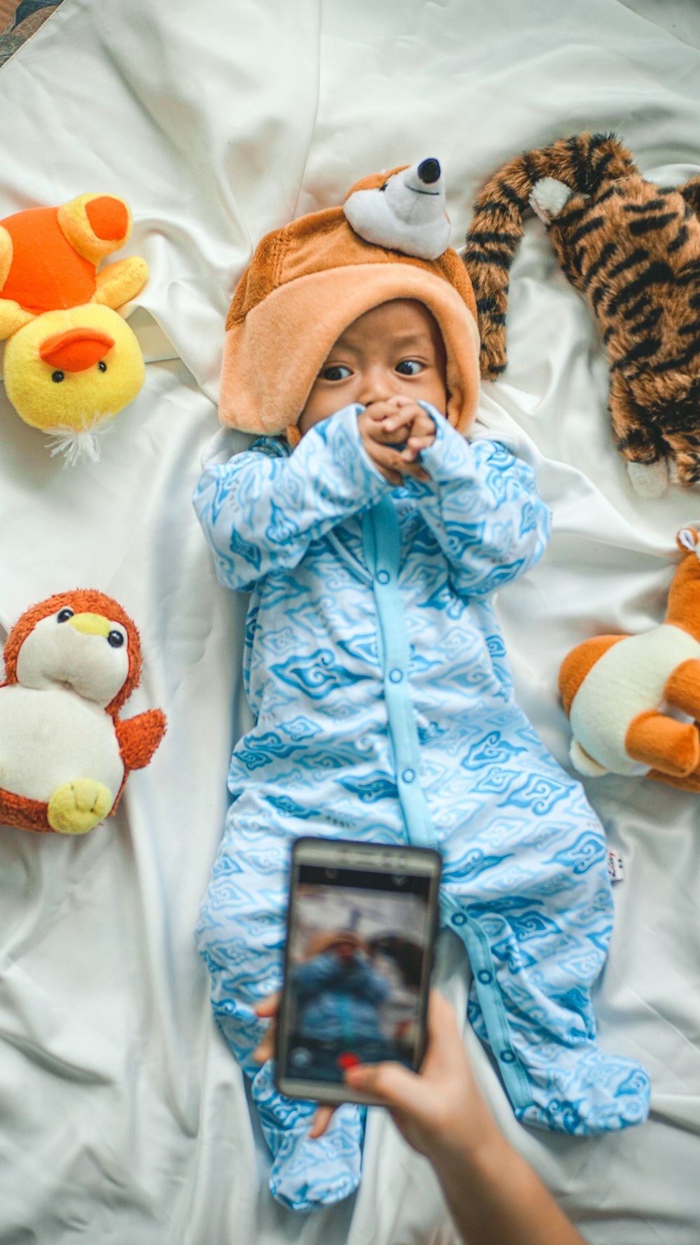 baby in blue jacket lying on white textile