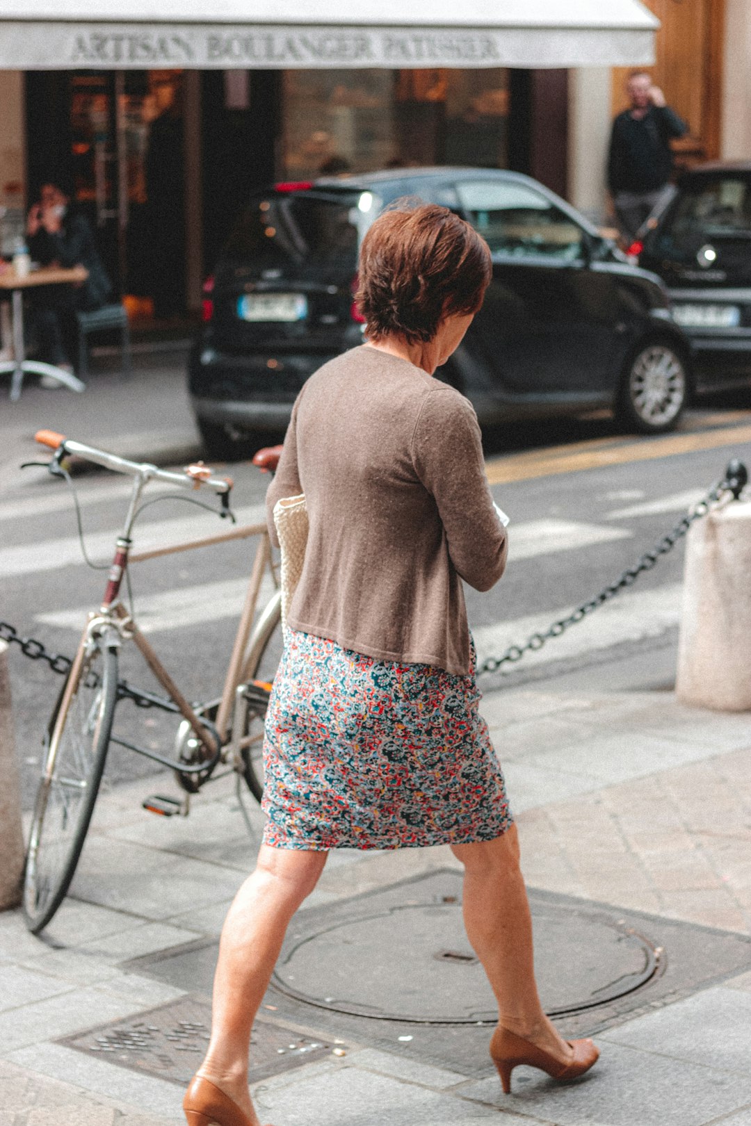 woman in brown long sleeve shirt and blue and white floral skirt standing on sidewalk during