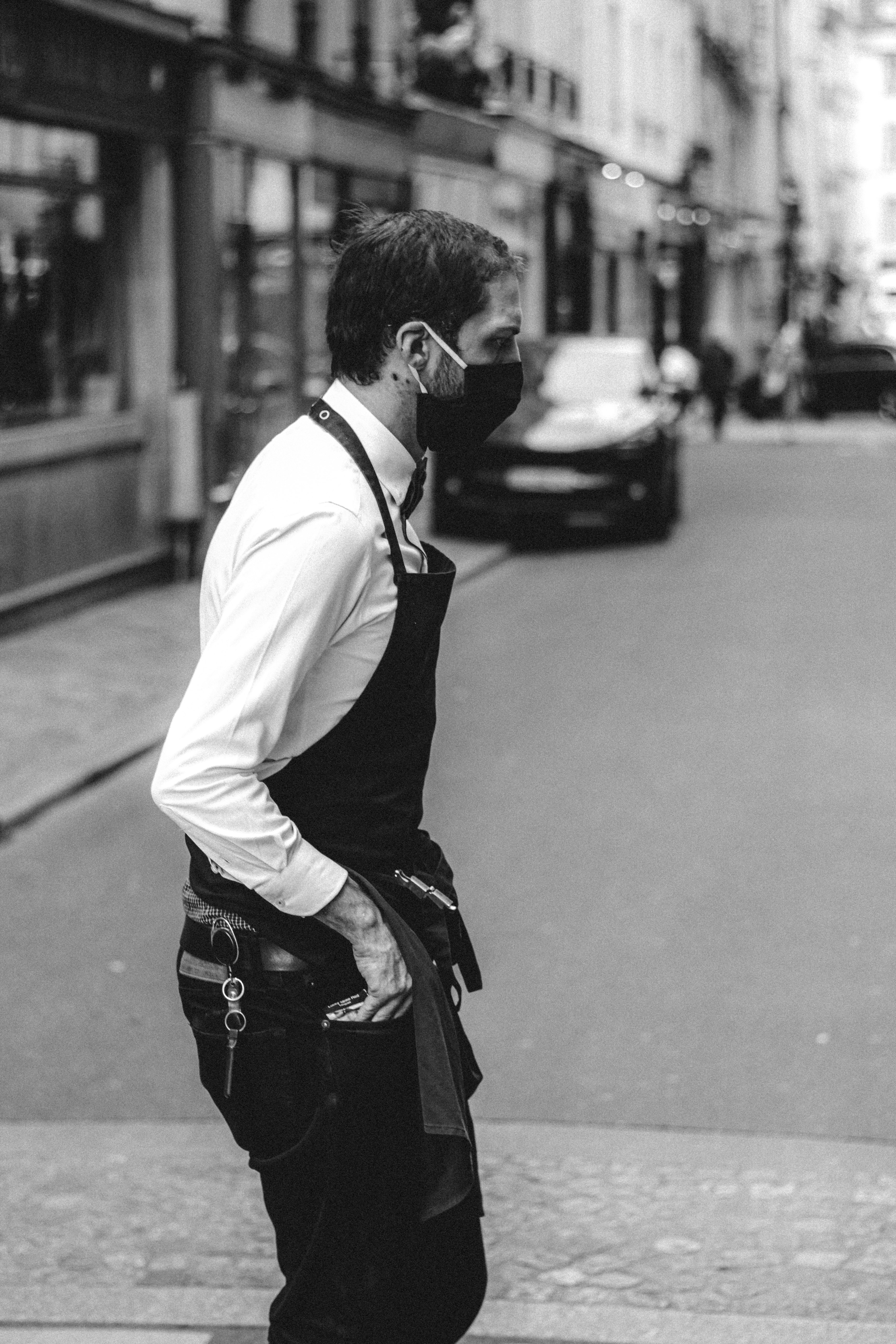 man in white dress shirt and black dress pants standing on sidewalk in grayscale photography