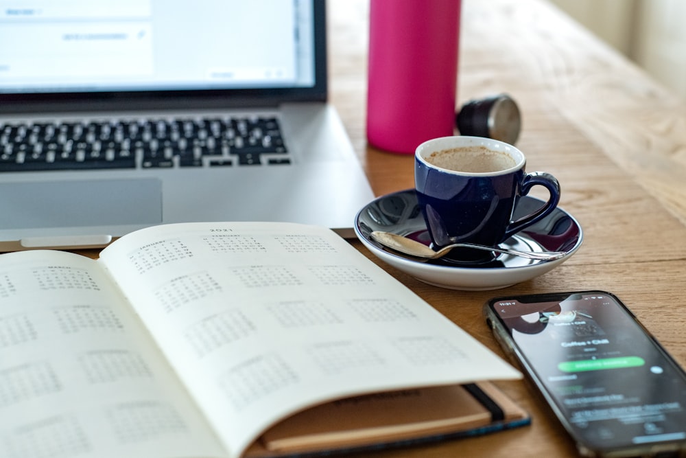 black and white ceramic mug on saucer beside macbook pro