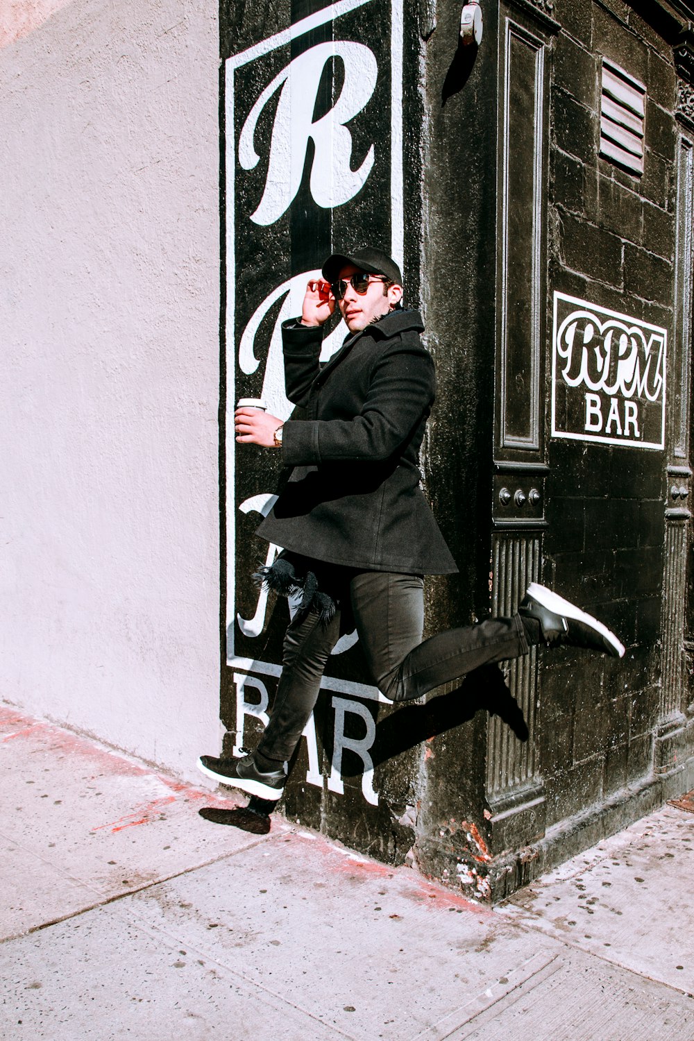 man in black jacket and black pants wearing black and white sneakers standing on sidewalk