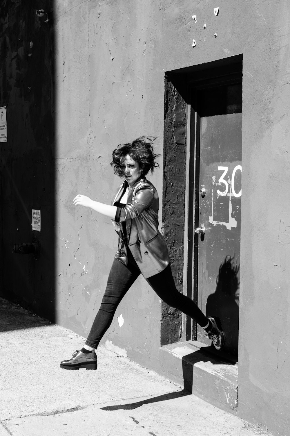 woman in white jacket and black pants leaning on wall