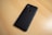 A black smartphone with a dual camera and fingerprint sensor on the back, placed on a light wooden surface.