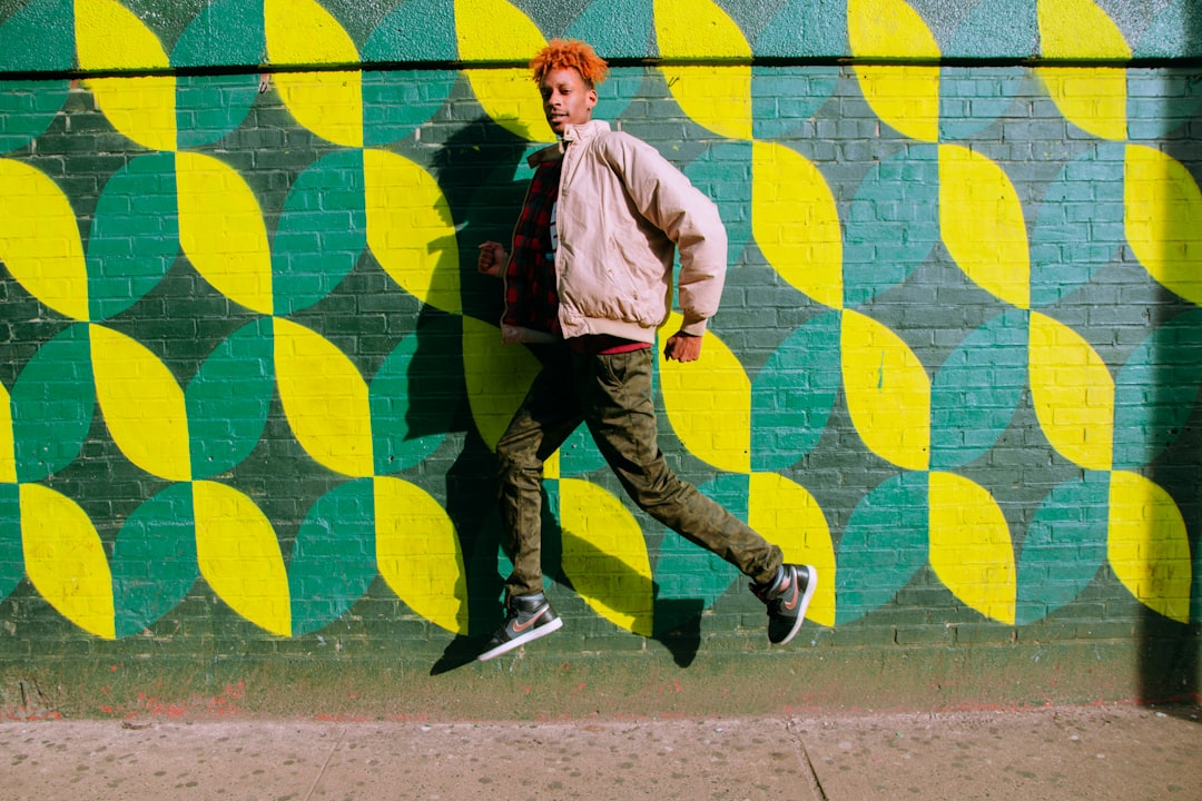 man in pink dress shirt and green pants walking on sidewalk during daytime