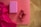 A yoga mat on a wooden floor with a vibrant pink cloth, a pink yoga block, and two red dumbbells placed on it.
