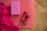 A yoga mat on a wooden floor with a vibrant pink cloth, a pink yoga block, and two red dumbbells placed on it.
