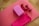 A wooden floor features a pink exercise mat laid out with assorted fitness equipment placed on top. A pink yoga block and a pair of small red dumbbells are neatly arranged. A folded pink towel rests beside them.