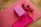 A wooden floor features a pink exercise mat laid out with assorted fitness equipment placed on top. A pink yoga block and a pair of small red dumbbells are neatly arranged. A folded pink towel rests beside them.