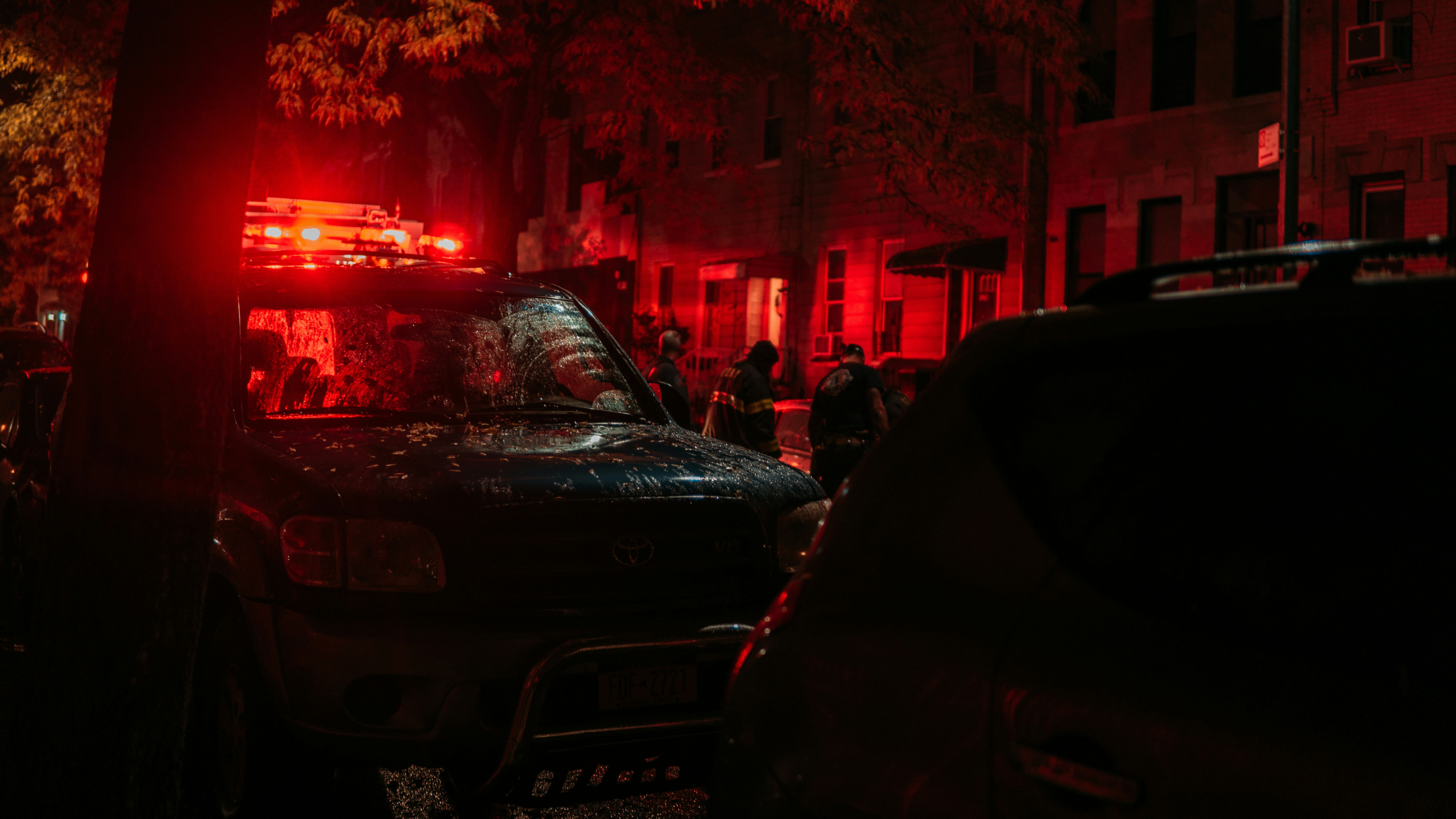 Emergency tow truck with flashing lights assisting broken down vehicle on dark urban street at night