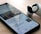 A smartphone on a wooden surface displays a Google News app with an article about George Floyd. Next to the phone, there is a pair of wireless earbuds in a partially opened charging case.