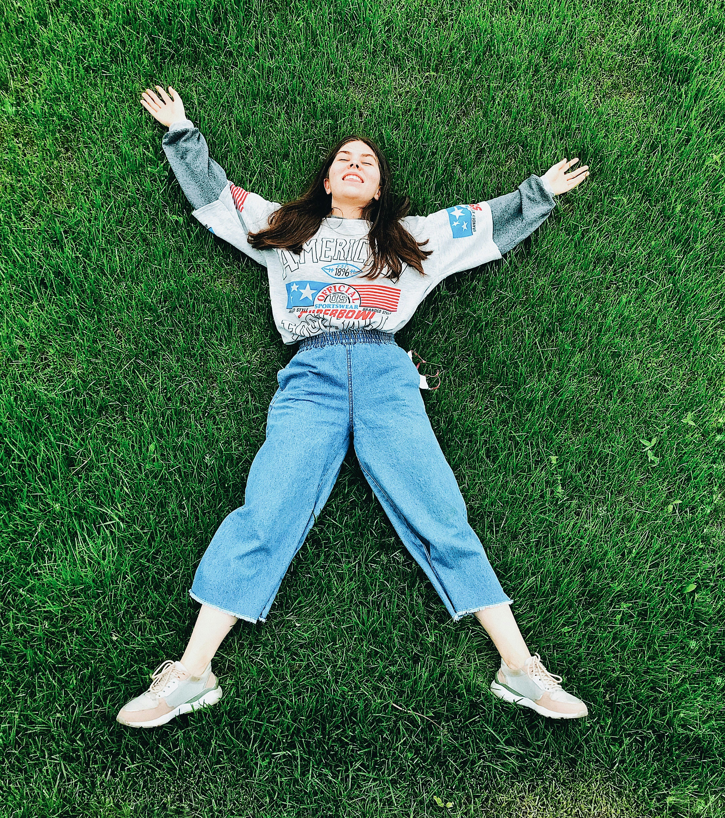 Frau in weißem Langarmhemd und blauer Jeans liegt auf grünem Rasen während