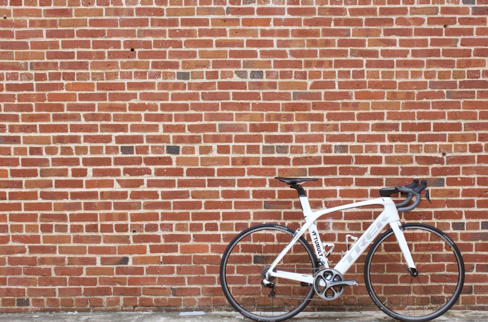 white and black road bike leaning on brown brick wall