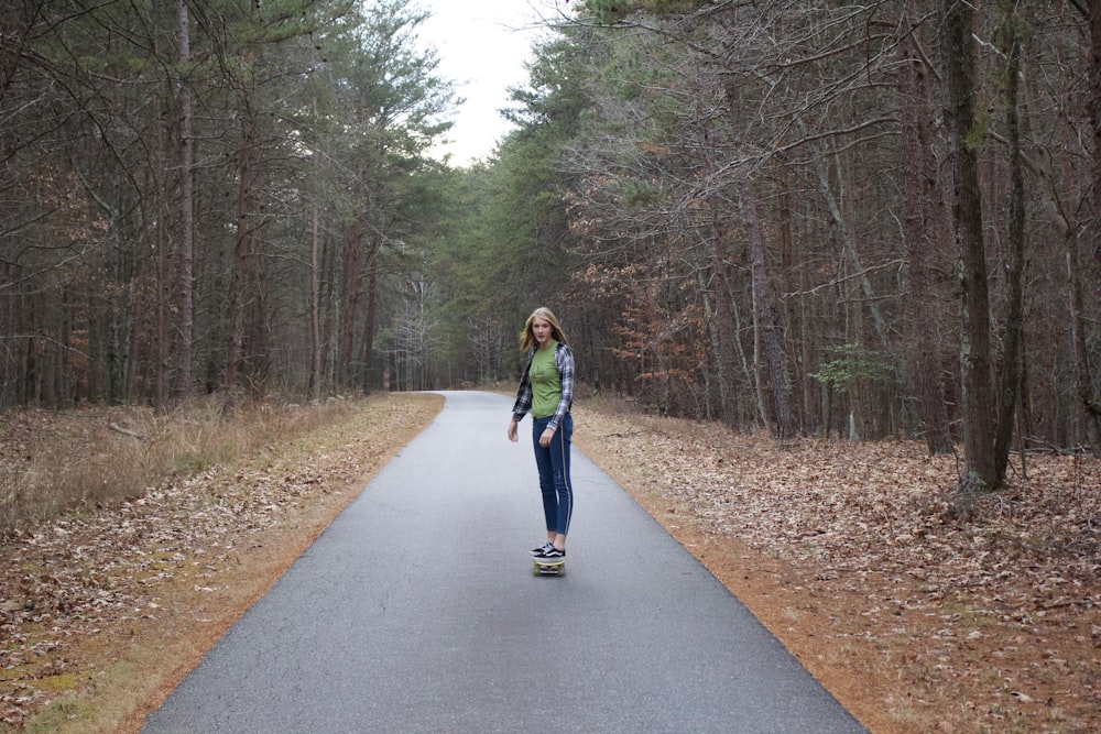 woman in blue jacket standing on gray asphalt road between trees during daytime