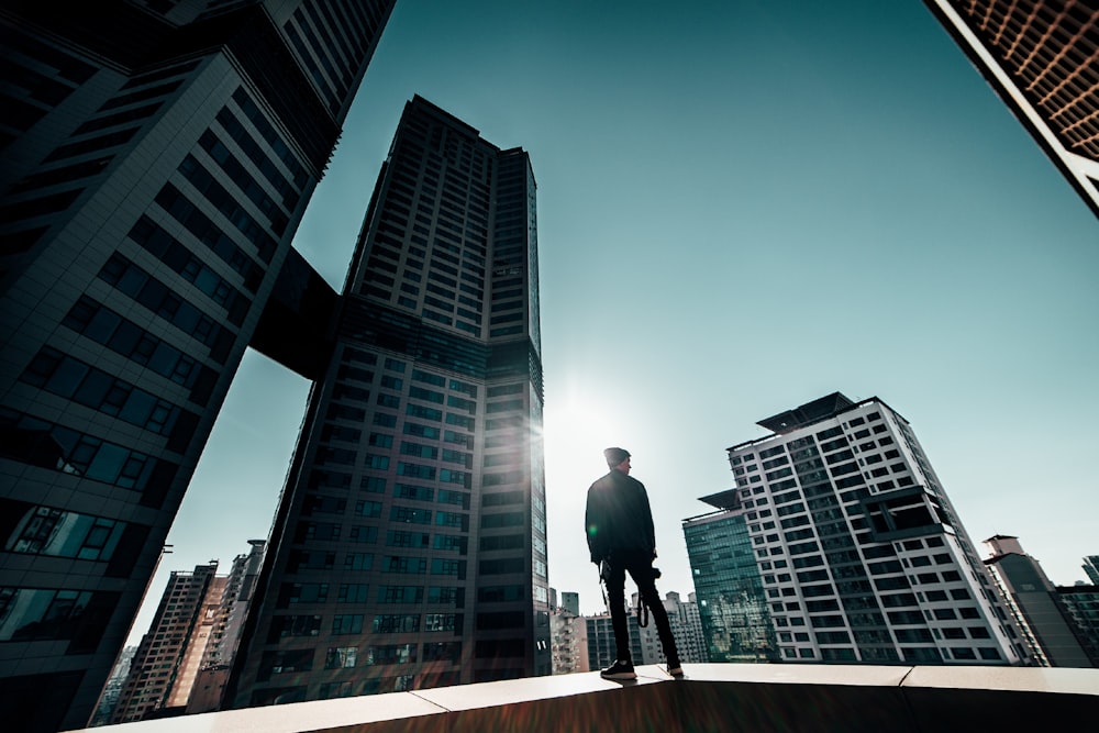 man in black jacket and pants walking on sidewalk near high rise buildings during daytime