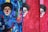 The image features a vibrant and abstract painting of clowns with exaggerated makeup and big red noses. The background is composed of swirling patterns in deep blues and reds, with some areas of green and yellow. The clowns are accentuated by stark black hair and facial features, creating a bold contrast against the colorful backdrop.