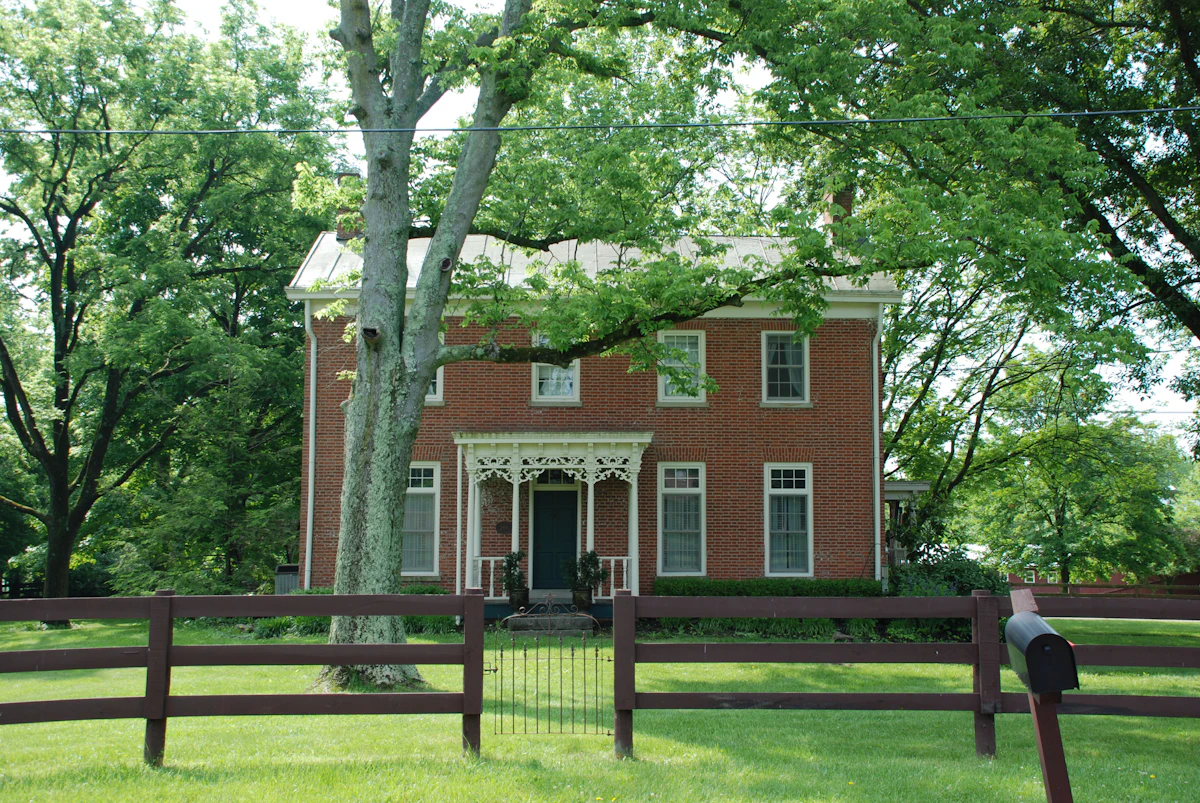 Historic brick home with white trim, an ornate porch and a rail fence