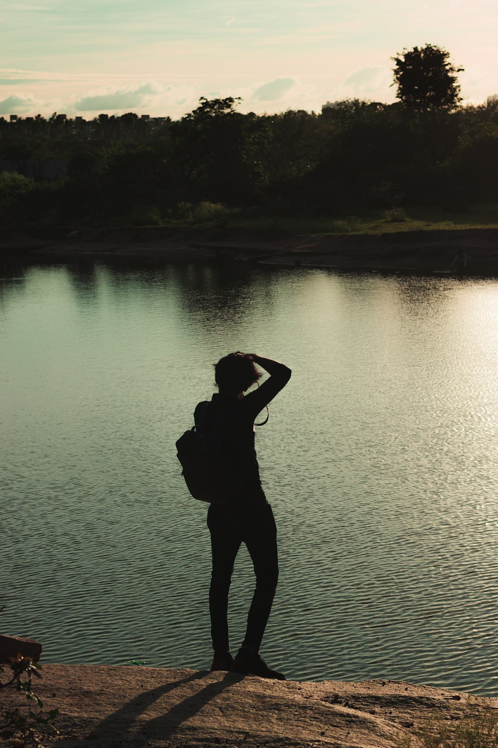 silhouette of woman standing on lake shore during daytime