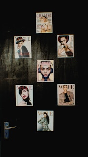 A collection of magazine covers is displayed on a dark wall, each featuring a different portrait of a person. The covers are from well-known fashion magazines such as Vogue, Grazia, and Elle. The arrangement is aesthetically pleasing and suggests a focus on fashion and style.