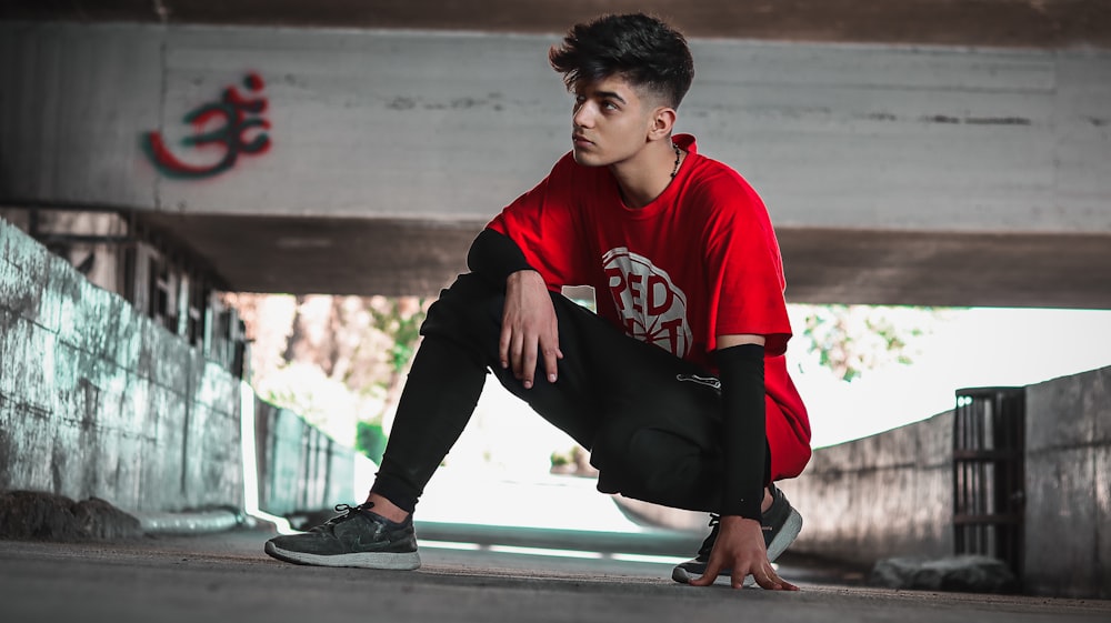 man in red and white hoodie and black pants sitting on concrete bench during daytime
