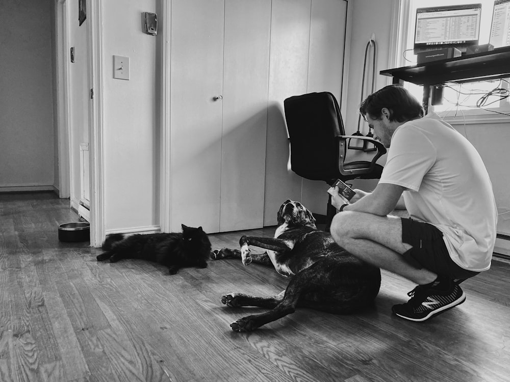 man in white t-shirt sitting beside black short coated dog