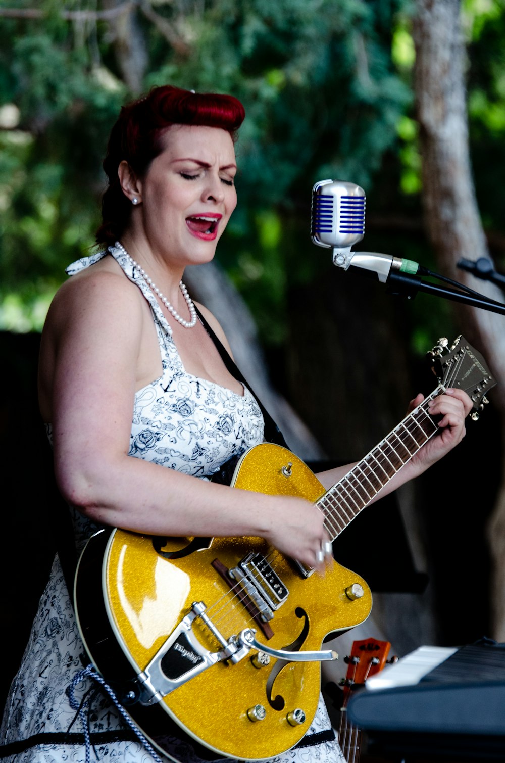 smiling woman in white floral sleeveless top holding yellow electric guitar