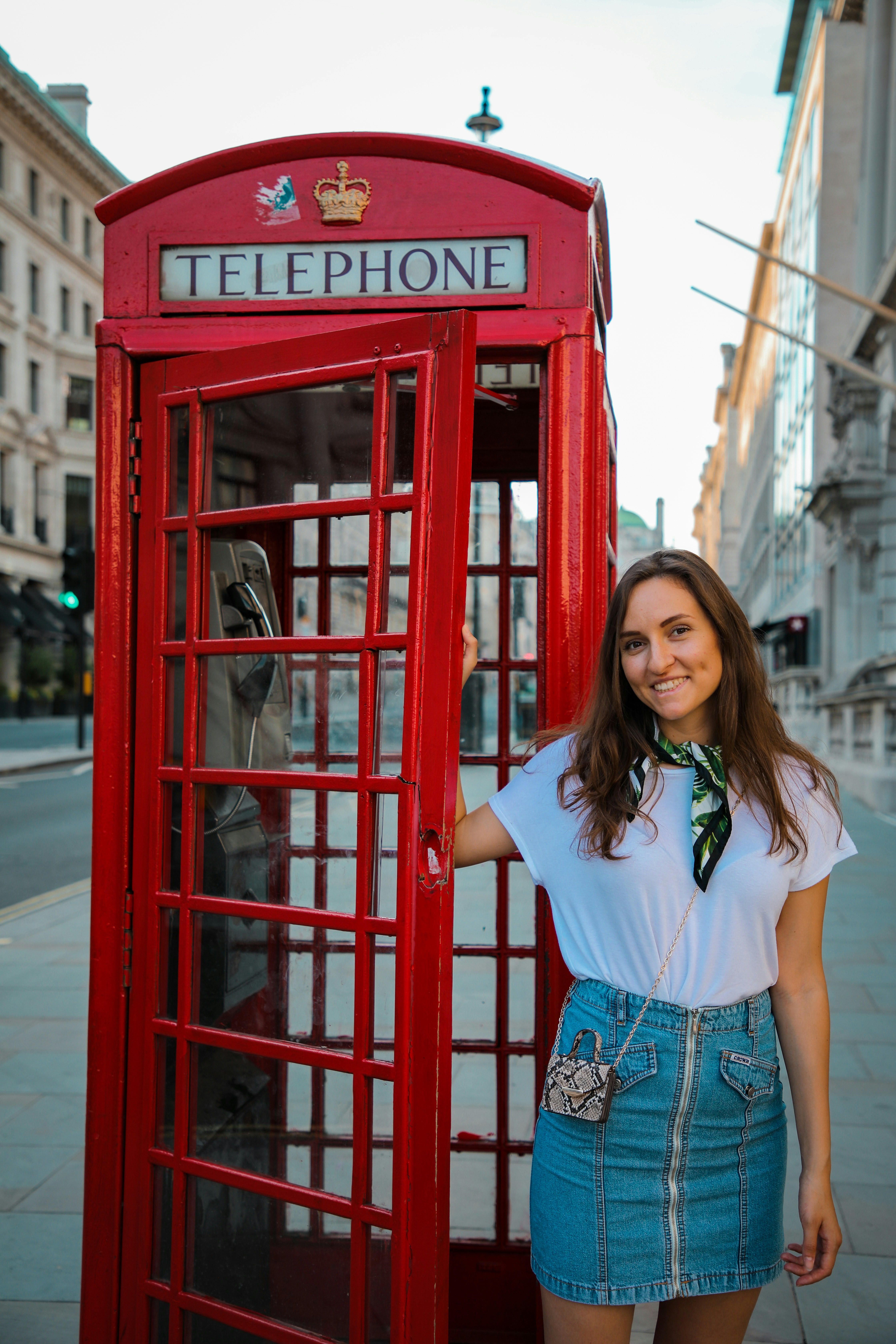 woman in white shirt and blue denim shorts standing beside red telephone booth during daytime