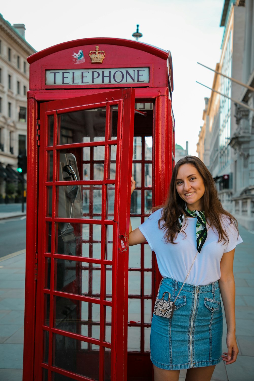 woman in white shirt and blue denim shorts standing beside red telephone booth during daytime