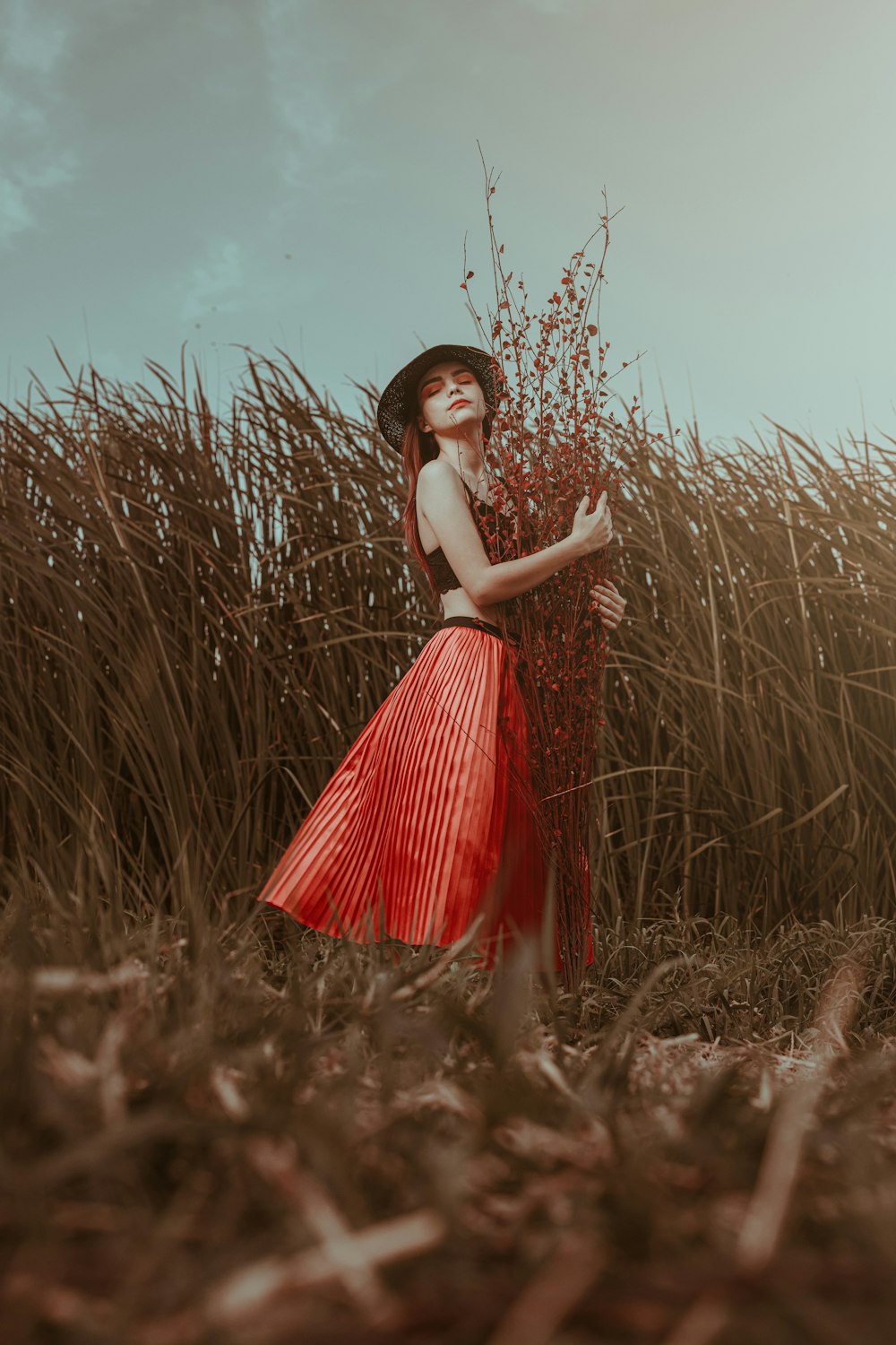 Femme en robe rouge et blanche debout sur le champ d’herbe brune pendant la journée