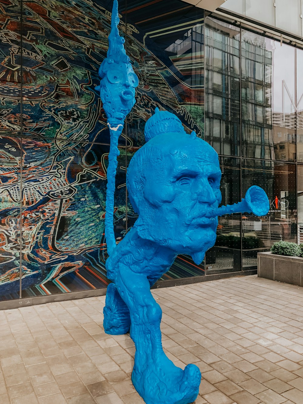 a blue sculpture of a man holding a stick in front of a building