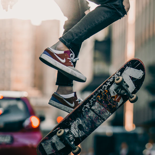 A skater in black pants and black and white sneakers jumping on a skateboard