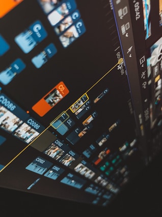 A close-up view of a video editing timeline on a computer screen with multiple video clips and tracks. Blue and orange clips are organized in a diagonal layout, and various icons and controls are visible on the interface.