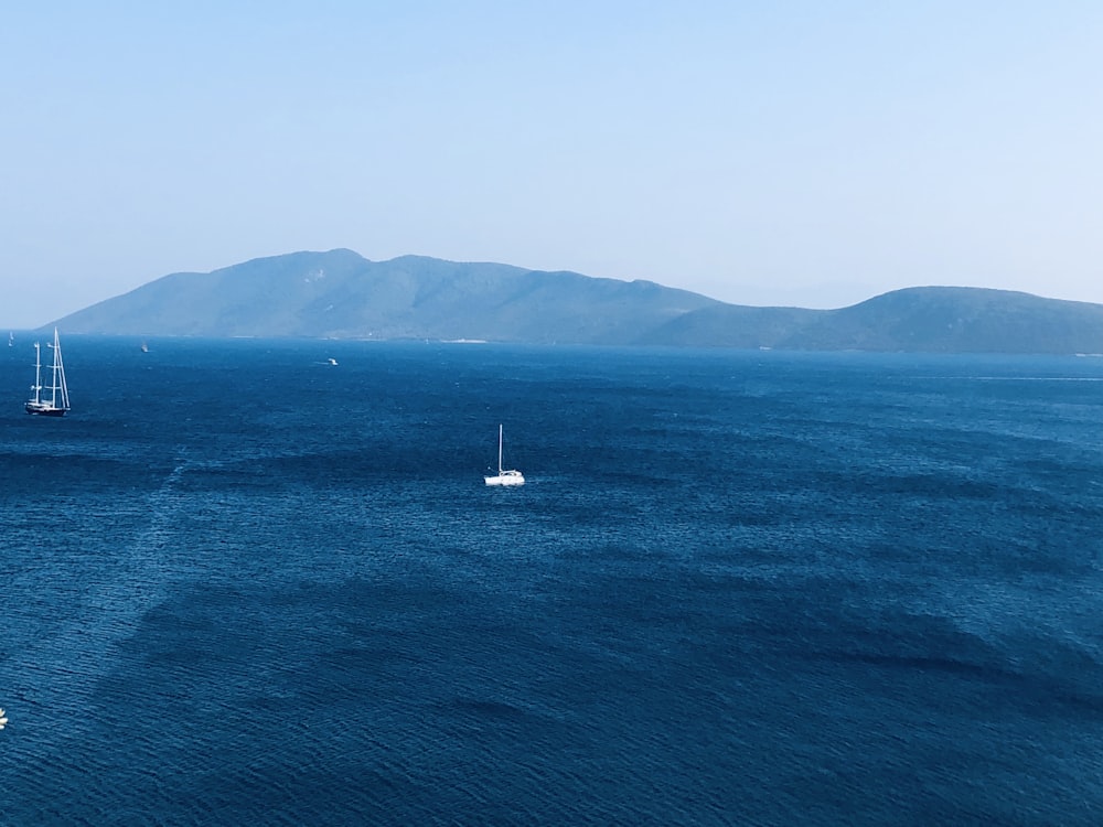 white sailboat on sea near green mountain during daytime
