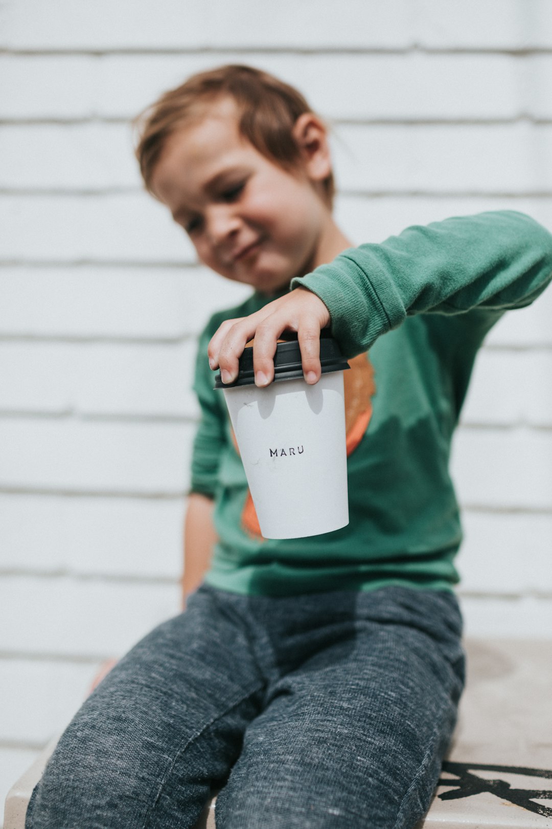 boy in green long sleeve shirt holding white plastic cup