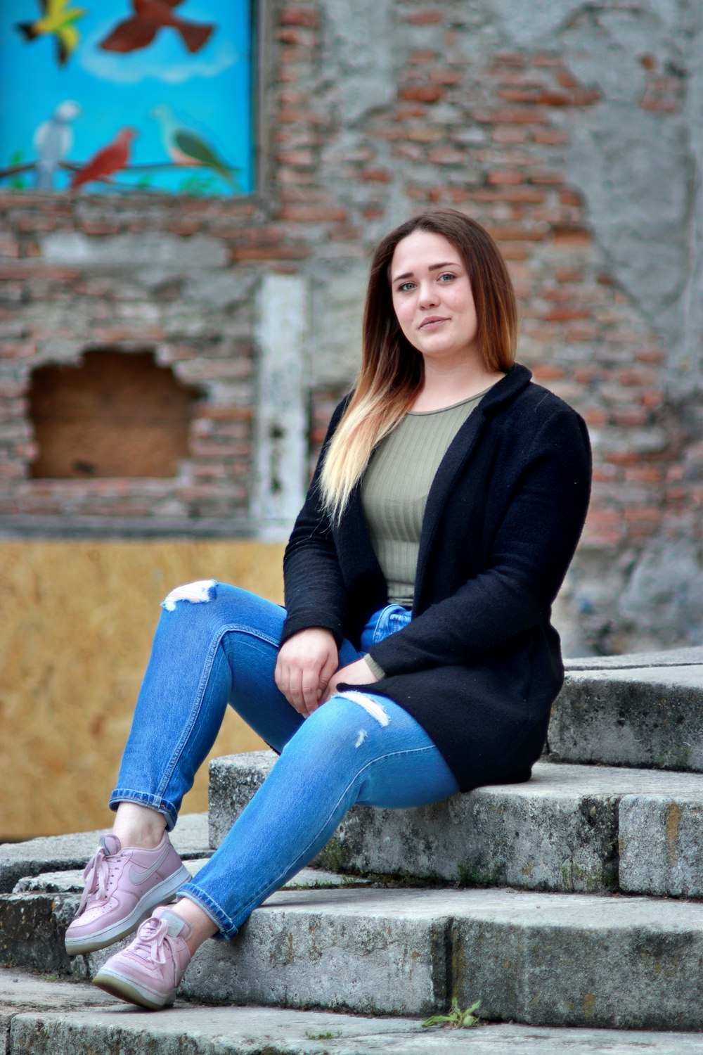 woman in black cardigan and blue denim jeans sitting on concrete wall during daytime