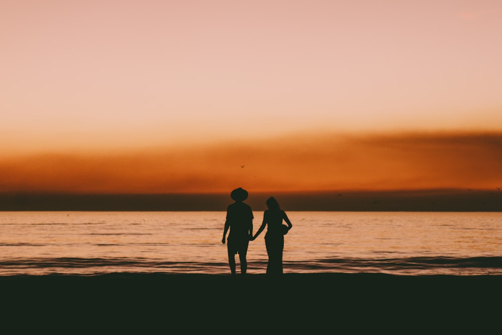 夕暮れ時のビーチで手をつないでいるカップルのシルエット