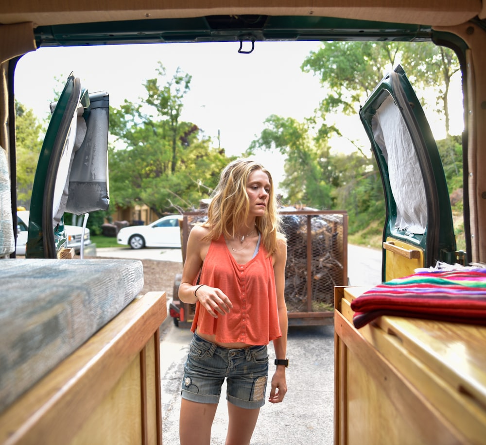 woman in orange t-shirt and blue denim shorts standing beside brown wooden table