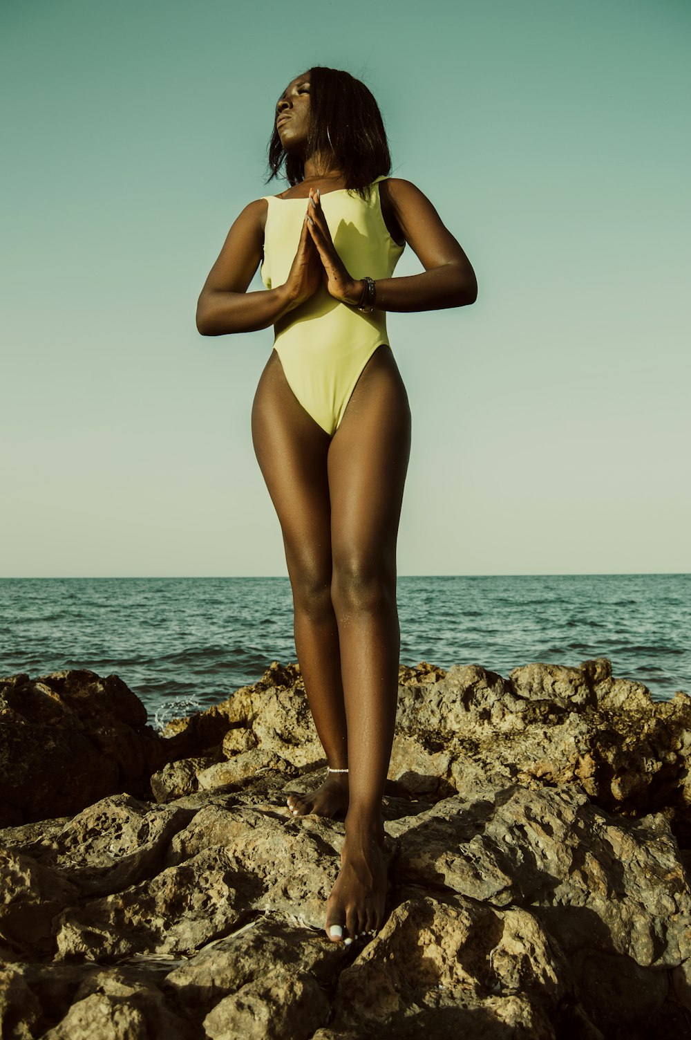 woman in white one piece swimsuit standing on rocky shore during daytime