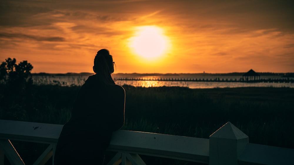 une personne assise sur une clôture regardant le coucher du soleil