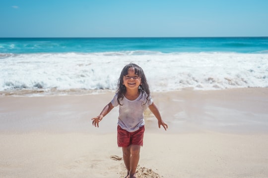 girl in white tank top and blue denim shorts standing on beach during daytime in Dreamland Beach Indonesia