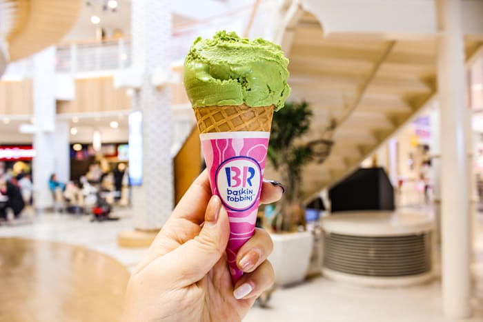 A hand holding a Baskin Robbins ice cream, cone, green ice cream