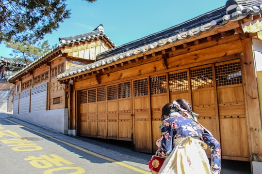 woman in white and brown floral dress standing on gray concrete road during daytime in Bukchon Hanok Village South Korea