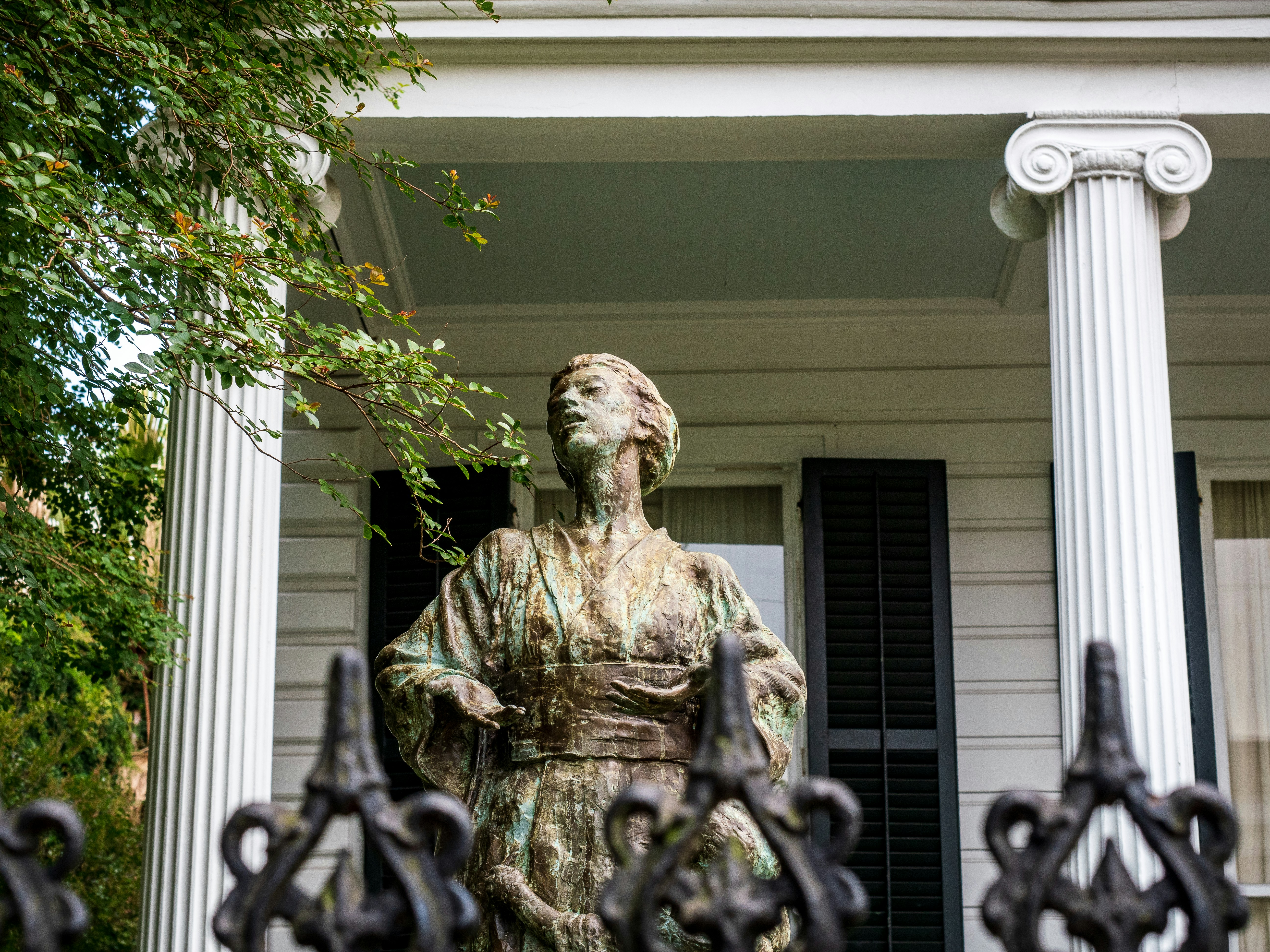 Statue of a woman in front of a Garden District home with columns