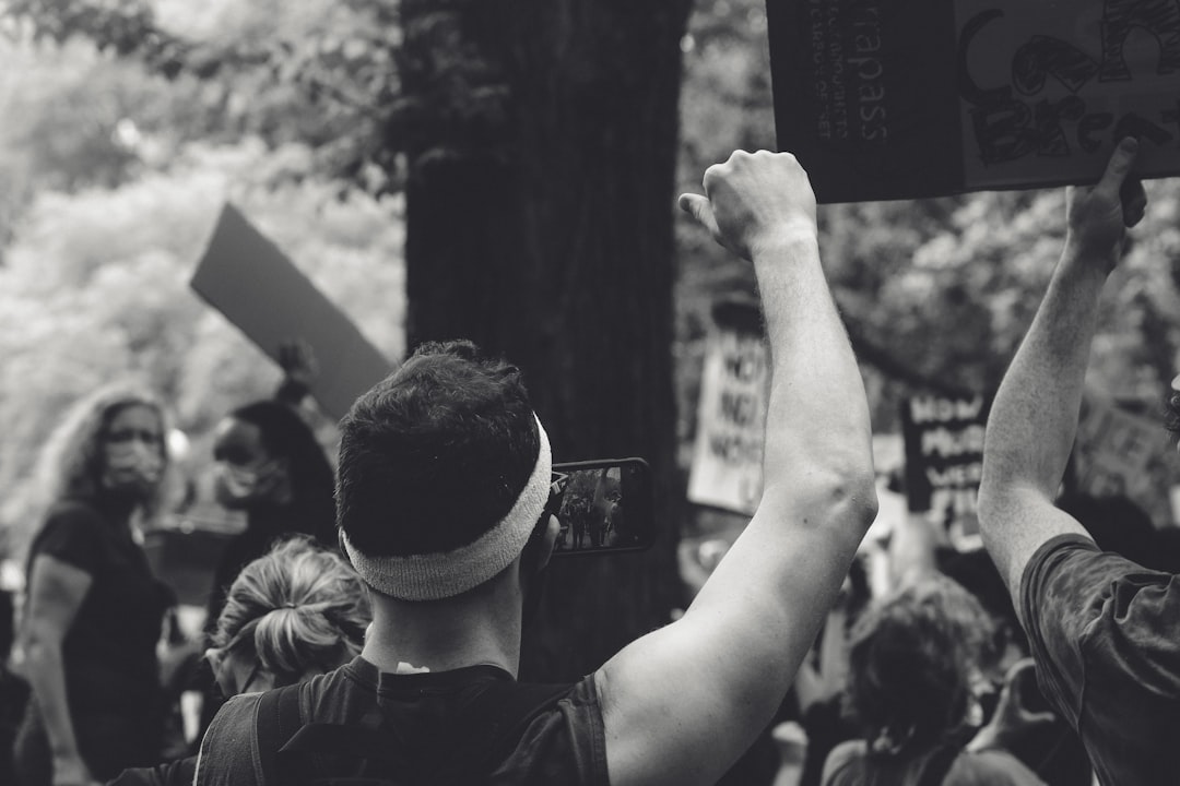 grayscale photo of man in black shirt raising his hand