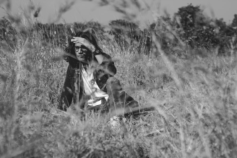 woman in black coat sitting on grass field in grayscale photography
