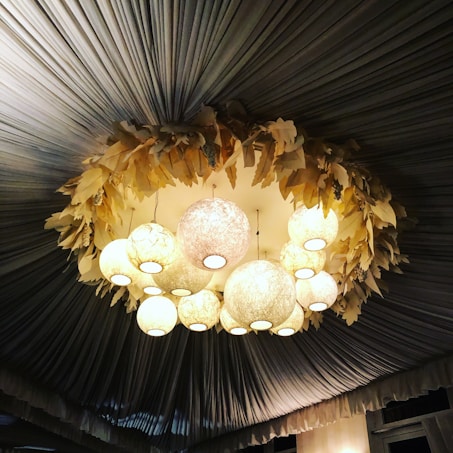 A ceiling adorned with a decorative arrangement featuring soft glowing spherical lights and a wreath-like structure with leaf-shaped elements. The draped fabric ceiling panels create a luxurious and elegant atmosphere.
