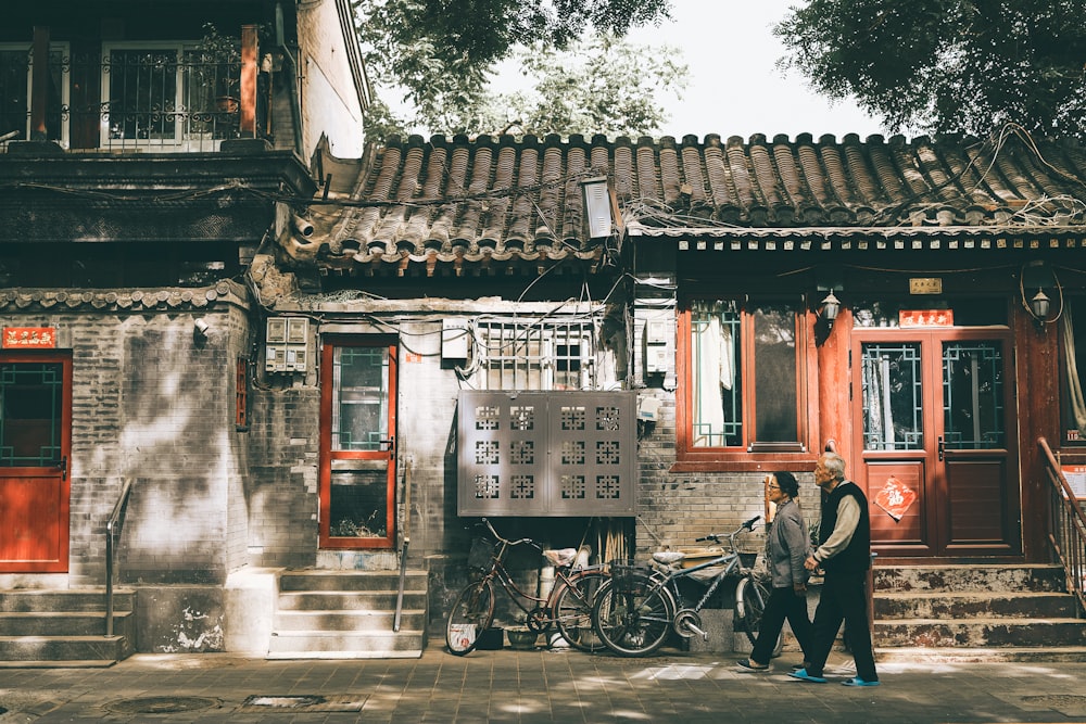 man in black jacket standing beside bicycle near red wooden door during daytime